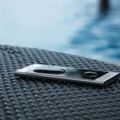 Smartfon z kroplami wody na ekranie, leżący na plecionej powierzchni. IP68 co oznacza? To wodoodporność, idealny na wakacje przy basenie.