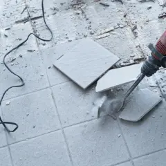 Skuwanie płytek młotem udarowym. Widać kurz i fragmenty materiału.