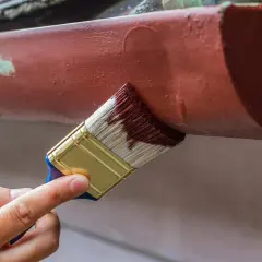 Ręka maluje pędzlem rynny, odnawiając je. Dowiedz się, czym pomalować aluminium, by wyglądało jak nowe.
