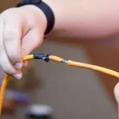 Dłonie trzymają przerwany pomarańczowy kabel, pokazując, jak połączyć przerwany kabel.
