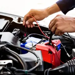Mechanik sprawdza, jak sprawdzić co pobiera prąd w samochodzie, mierząc napięcie na akumulatorze.
