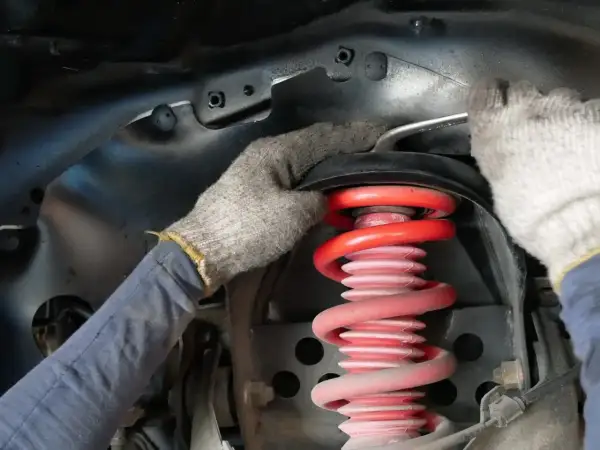 Mechanik w rękawiczkach dokonuje wymiany sprężyny amortyzatora w samochodzie.