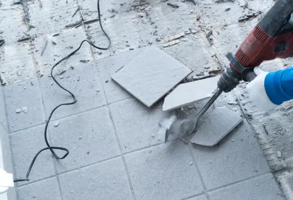 Skuwanie płytek młotem udarowym. Widać kurz i fragmenty materiału.
