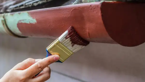 Ręka maluje pędzlem rynny, odnawiając je. Dowiedz się, czym pomalować aluminium, by wyglądało jak nowe.