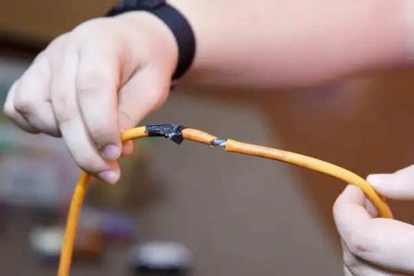 Dłonie trzymają przerwany pomarańczowy kabel, pokazując, jak połączyć przerwany kabel.